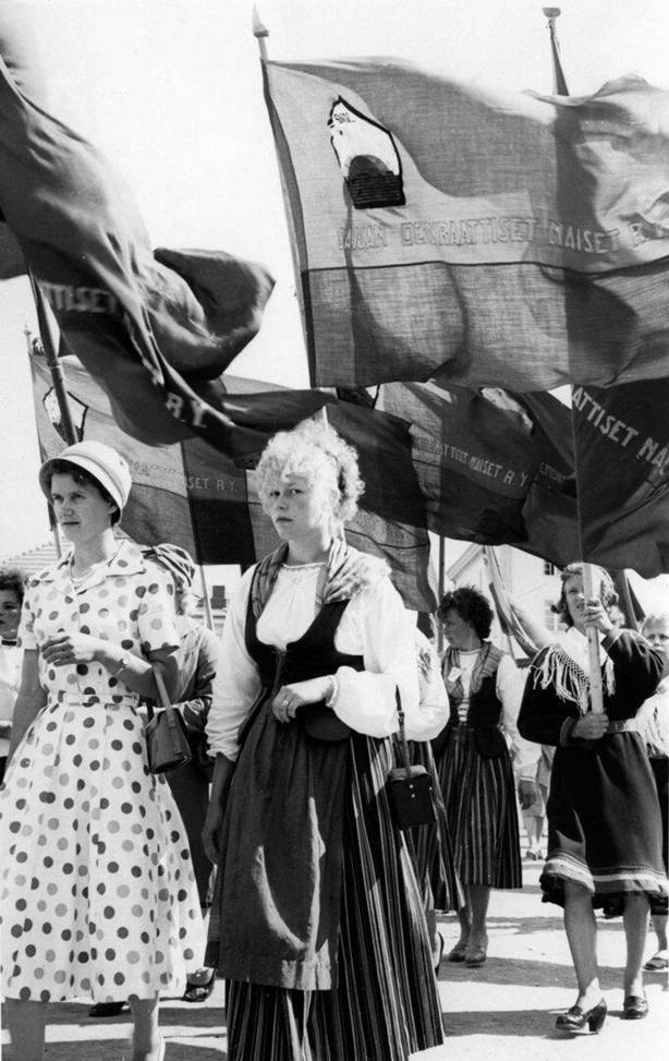 Kansallispukuisia naisliittolaisia kulkueessa järjestölippuineen
(Kuva: Kansan Arkisto)